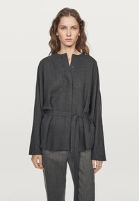 Kolkgray långärmad blus med hög krage, kn�äppning fram och knytning i midjan. Texturerad tyg och avslappnad passform.