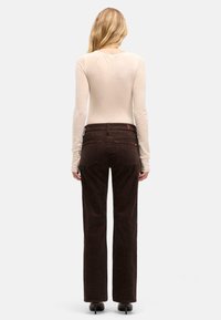 Pantaloni in corduroy marrone con taglio dritto e tasche posteriori, abbinati a un top aderente a maniche lunghe. Dettagli minimi e texture liscia.