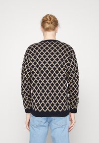 Maglione a maglia con motivo geometrico beige su sfondo blu navy. Maniche lunghe e scollo rotondo, con polsini e orlo a coste.