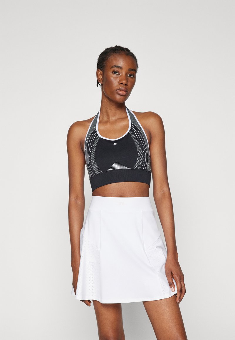 Svart atletisk crop topp med hvite detaljer og geometriske mønstre, sammen med en hvit skort som har perforerte detaljer og lommer.
