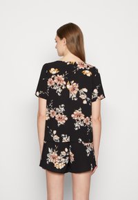 Top preto de flores com mangas curtas, apresentando flores em rosa e branco, um corte descontraído e uma textura suave, combinado com calções pretos iguais.