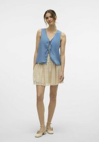 Blå ärmlös topp med en knytning fram, matchad med en krämfärgad spetskjol med blommönster och en scallopad fåll.