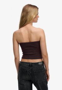 Strapless ribbed crop top in dark gray with maroon stripes; fitted design with a smooth texture. Worn with high-waisted black jeans.