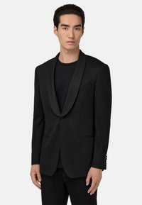 Svart blazer med satin sjalkrage, enkel knappstängning, två framfickor och skräddarsydd passform. Bärs över en svart skjorta.