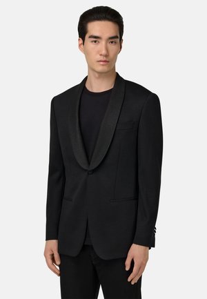 Zwarte blazer met een satijnen sjaalkraag, enkele knoopsluiting, twee voorkruiken en een getailleerde pasvorm. Draag over een zwart shirt.