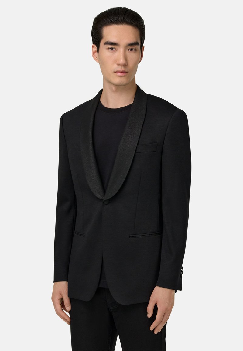 Svart blazer med satin sjalkrage, enkel knappstängning, två framfickor och skräddarsydd passform. Bärs över en svart skjorta.