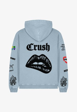 Svijetloplava dukserica s velikim crnim izvezenim motivom usana i tekstom "Crush". Akcenti i vezice u raznim bojama na rukavima.