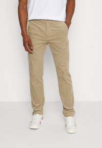 Beige kordfläskbyxor med raka ben, med ett strukturerat ribbat mönster och standardfickor, parat med vita sneakers.