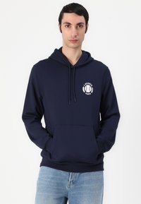 Felpa blu navy realizzata in tessuto morbido, con tasca frontale e logo Lacoste bianco con accenti di alloro sul petto.