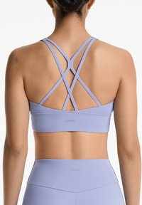 Svijetl Lavender sportski grudnjak s dizajnom remenja u obliku križa, bešavnog završetka i logotipom na traci. Izrađen od rastezljivog, glatkog materijala.