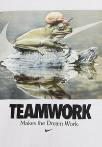 Camiseta blanca con un gráfico de una rana verde con un caracol en la cabeza sentada sobre una tortuga, acompañada del texto "EL TRABAJO EN EQUIPO HACE QUE EL SUEÑO FUNCIONE."