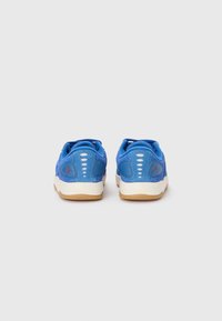 Baskets bleues avec une tige en daim et en maille, présentant des accents blancs, un col rembourré et une semelle en caoutchouc. Logo notable au niveau du talon.
