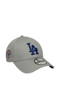 Gorra de béisbol gris con un logo bordado azul "LA", corona redondeada, correa ajustable y un emblema circular de los Dodgers en el lado.