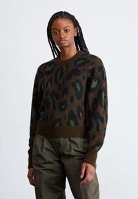 Gebreide trui in donkerbruin met een luipaardprint met groene en zwarte accenten. Geribbelde mouwen en zoom, ronde hals, relaxte pasvorm.