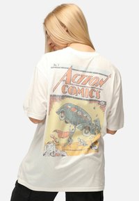 Weißes Oversized-T-Shirt mit einem Retro-Comics-Druck auf der Rückseite, das ein grünes Auto und Charaktere in Aktion zeigt. Aus weichem Baumwollmaterial.