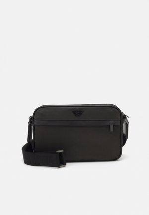 Sac bandoulière rectangulaire noir avec bandoulière réglable, poche zippée à l'avant et logo en relief au centre supérieur.