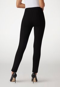 High-waisted black leggings featuring a fitted design with side seams and zippers at the ankle, made from a stretchy material.