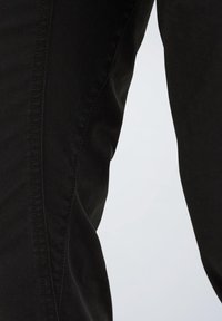 Črne denimske hlače z oprijeto zasnovo, gladko teksturo in subtilnim šivanjem ob stranskem šivu. Brez vidnih kovinskih delov ali vzorcev.