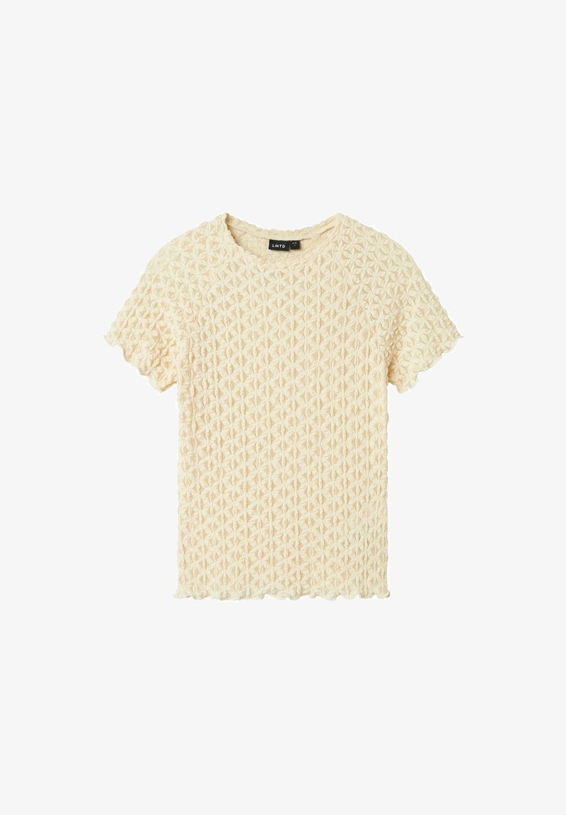 Haut à manches courtes de couleur crème avec un motif texturé en losanges et des bords en feston au niveau des manches et de l'ourlet. Le tissu semble tissé et léger.