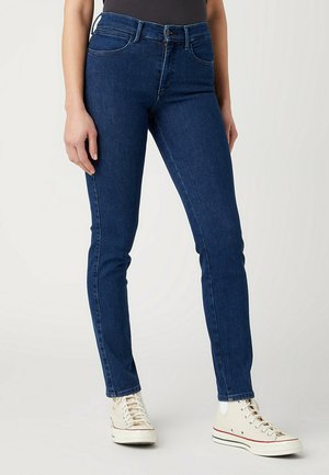 Jeans ajustados de color azul oscuro, fabricados en denim, con un diseño clásico de cinco bolsillos, trabillas para el cinturón, botón metálico y detalles de costura minimalistas.