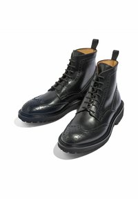Botas de tobillo de cuero negro con detalles de brogue, diseño de cordones, textura suave y suela de goma con un patrón de banda de rodadura contrastante.