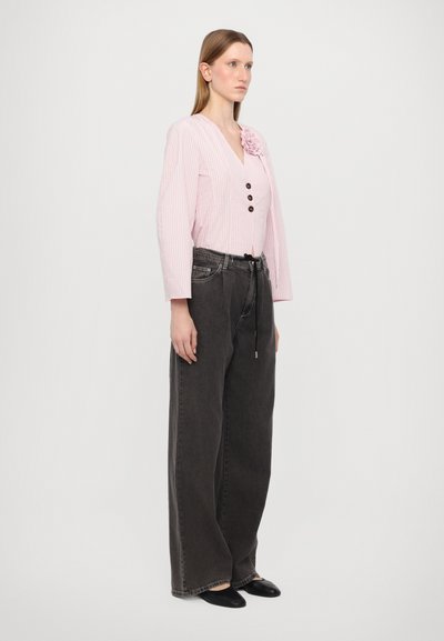 Ljusrosa randig blus med tre bruna knappar och en blom-dekoration, ihopparad med lösa svarta jeans och svarta platta skor.
