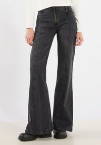 Pantalones vaqueros acampanados de mezclilla negra de tiro alto con costuras visibles, cremallera frontal y bolsillos laterales, que presentan un acabado de textura suave.