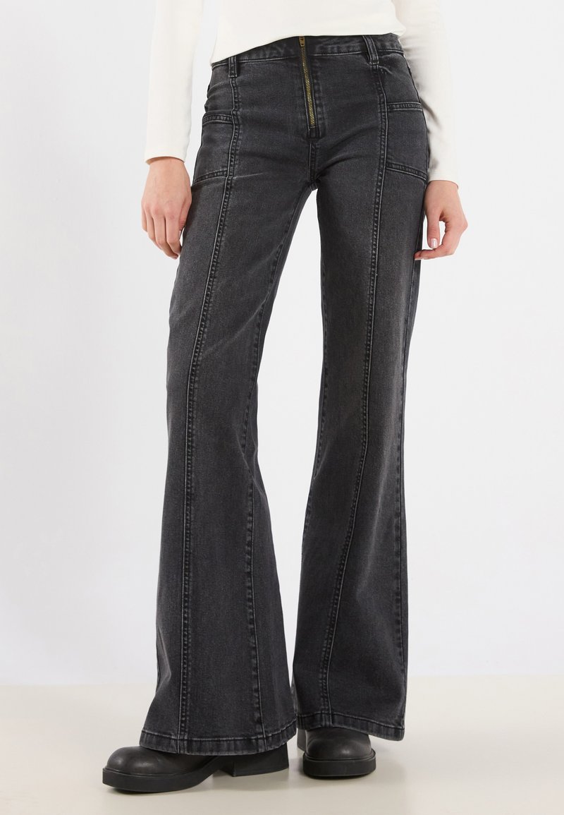 Pantalones vaqueros acampanados de mezclilla negra de tiro alto con costuras visibles, cremallera frontal y bolsillos laterales, que presentan un acabado de textura suave.