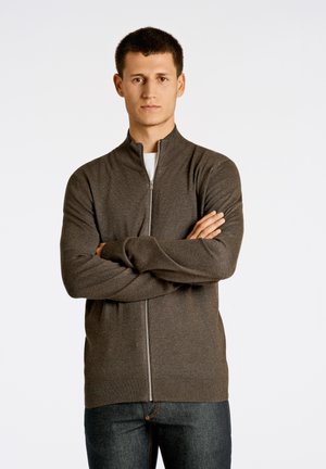 Mørkebrun lynlås sweater med høj krave, lavet af blødt stof, med ribbede manchetter og kant, båret over en hvid skjorte.