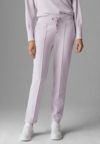 Ljuslila mjukisbyxor med dragsko i midjan, med veck fram, tillsammans med vita sportskor. Mjukt tyg.