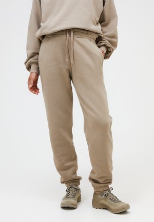 Person wearing beige sweatpants with drawstring waist and matching beige sneakers, standing against plain light background.