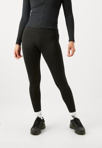 Leggings neri aderenti con una texture liscia, vita alta e scarpe da ginnastica nere abbinate a calzini bianchi alla caviglia.