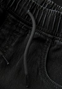 Juodai spalvotos laisvalaikio treniruoklių kelnės su elastinga juosta ir raišteliais, tekstūruota medžiaga bei sustiprintu siūlės viršutiniu kraštu.