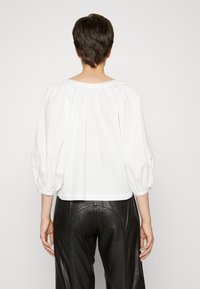 Weiße Bluse mit Puffärmeln, gerafftem Ausschnitt und lockerem Sitz. Kombiniert mit eng anliegenden schwarzen Lederhosen. Schlichte, glatte Textur.