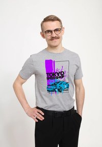 Šedé bavlněné tričko s obrázkem modrého sportovního auta, doplněné fialovými skvrnami a nápisem "TOKYO SPEED SHOP". Krátké rukávy, design s kulatým výstřihem.