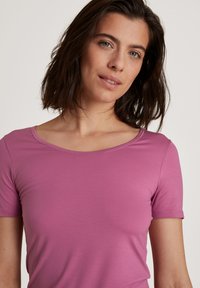Short-sleeve top in a solid, light purple fabric with a subtle ribbed texture and a wide neckline. Smooth finish, no visible patterns or accents.