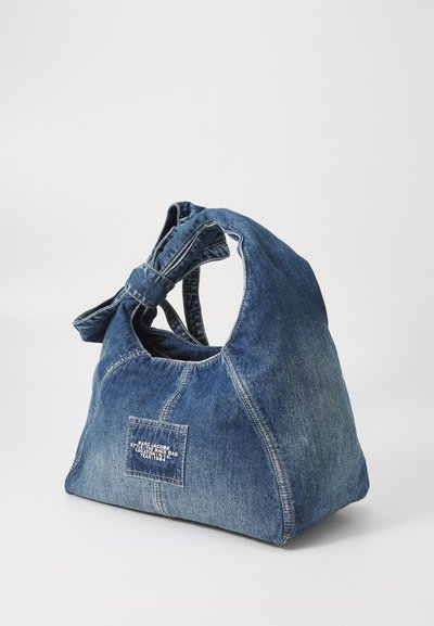 Borsa a spalla in denim con manico a nodo in cima, colore blu, corpo spazioso e tasca frontale con testo bianco.