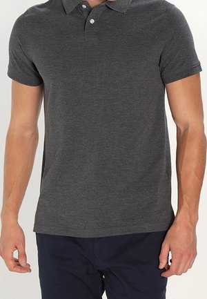 Homme portant un polo à manches courtes gris foncé et un pantalon bleu marine, debout les bras détendus le long du corps.