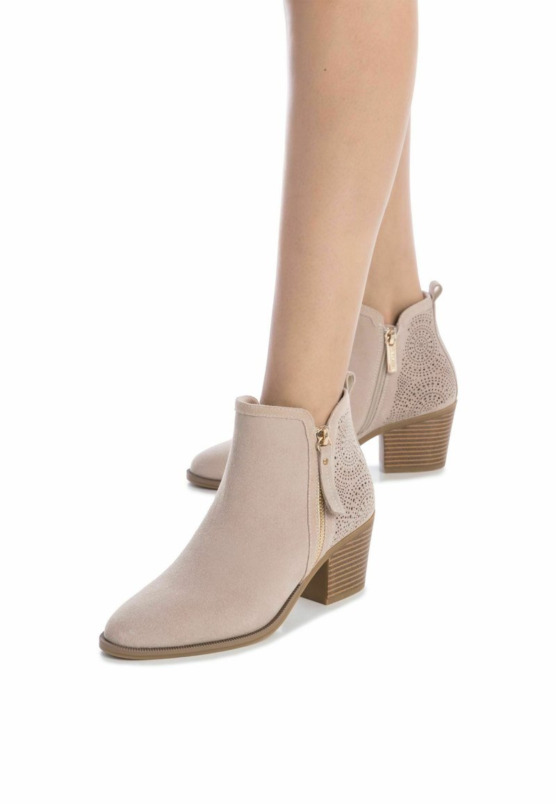 Botas de tobillo beige en suave ante con punta afilada, cremallera lateral y detalles perforados en la parte trasera; cuenta con un tacón apilado.