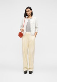 Heledad beežid kõrge vöökohaga püksid, hall soonikkoes topp, mustriline kerge kampsun, punane kott ja mustad kingad. Siledad tekstuurid ja lõdvestunud lõige.