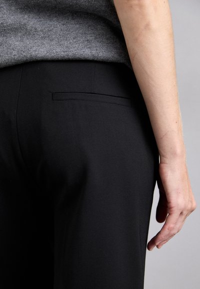 Black tailored trousers with a smooth texture, featuring a back pocket and a subtle seam detail. Gray knit top partially visible above waistband.