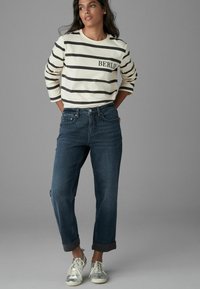 Sweatshirt en coton rayé crème et bleu foncé avec impression "BERLIN", associé à un jean bleu foncé. Manches retroussées et baskets argentées.