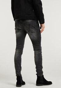 Jeans ajustados, de color negro desgastado con una textura suave, que incluyen bolsillos traseros y detalles de uso. Combinados con botines negros hasta el tobillo.