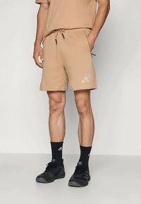 Bež kratke atletske hlače s elastičnim pojasom i vezicom. Imaju Adidas logo u svjetlijoj nijansi. Nosi se s crnim čarapama i cipelama.