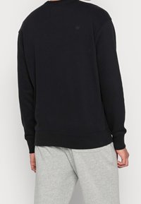 Černý crewneck svetr s dlouhými rukávy, volným střihem, žebrovanými manžetami a lemem. Tkanina vypadá měkce a nemá viditelné logo ani vzory.