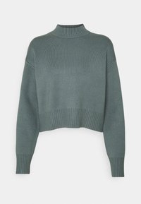 Krótki sweter w stonowanej zieleni, z prążkowanym półgolfem i mankietami, wykonany z miękkiego dzianinowego materiału; ma luźny krój i teksturowaną powierzchnię.