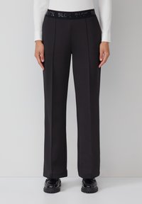 Pantalons larges noirs avec une taille élastique texturée arborant un détail « BLCK » en relief, fabriqués à partir d'un tissu lisse avec des plis latéraux.
