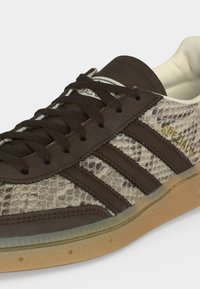 Καφέ sneaker Adidas με υφή φιδιού, μαύρες ρίγες, λαστιχένια σόλα και χρυσό κείμενο "SPEZIAL" στο πλάι.