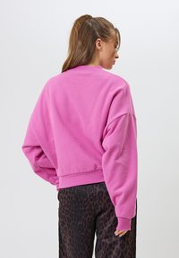 Fuksia vaaleanpunainen collegepaita, jossa on rento istuvuus, ribbireunainen kaula-aukko ja lasketut hartiat, yhdistettynä mustiin leopardikuvioisiin housuihin.