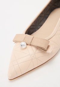 Ballerine pointue de couleur pêche avec texture matelassée, accent en bande élastique et détail en perle. Tige en cuir souple avec intérieur lisse.